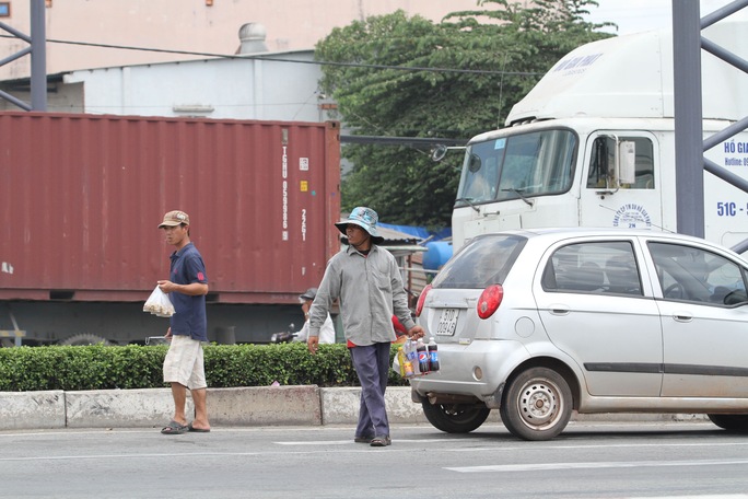 Giữa dòng xe container, xe tải, những người này cố gắng luồn lách để bán từng chai nước, bịch đậu phộng