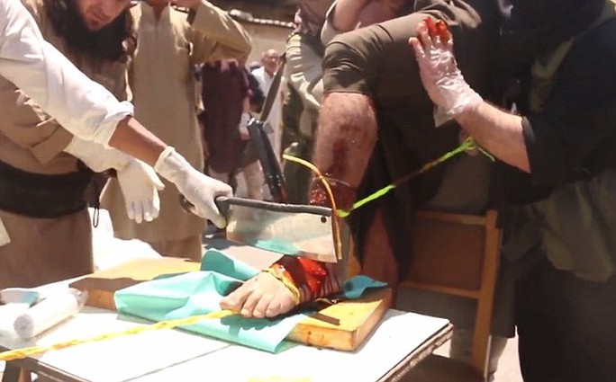 Cruel: The first mans foot is covered in what appears to be red antiseptic solution before an ISIS militant chops off his foot with a meat cleaver