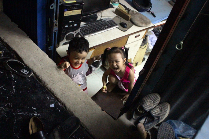 
Hai đứa trẻ chơi đùa trước cửa nhà, trong không gian bức bối
