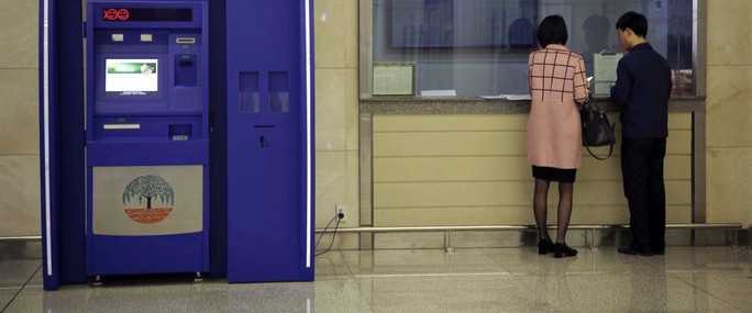 
Một người đàn ông và phụ nữ đứng ở quầy bên cạnh ATM của Ngân hàng Thương mại Ryugyong tại Aân bay quốc tế Sunan. Ảnh: AP
