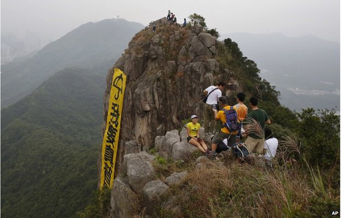 Hikers take pictures of the yellow banner with the words reading: I want genuine universal suffrage in Chinese and Umbrella Movement in English hanging from the face of Lion Rock mountain in Hong Kong Thursday, 23 October 2014