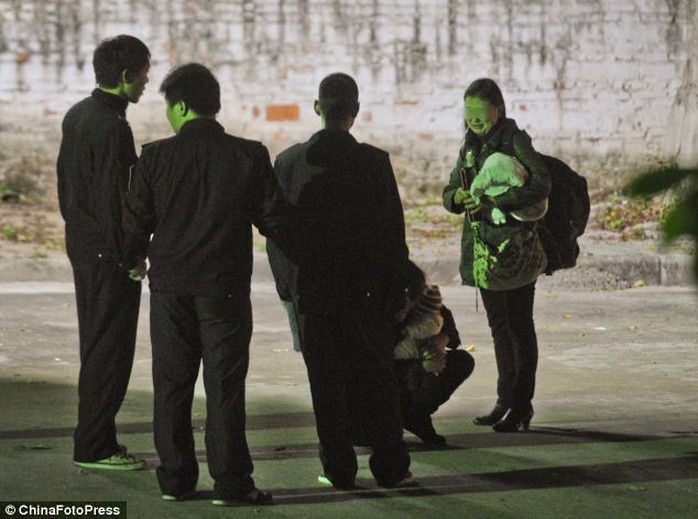 A woman holding her  baby, who has Downs syndrome, crouches and cries between security guards and a family member in front of the Guangzhou baby hatch