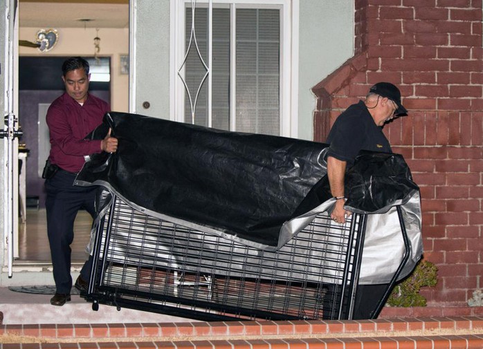 A crime scene investigator and a detective carry a cage from a home. Police say parents kept their 11-year-old autistic son locked inside.