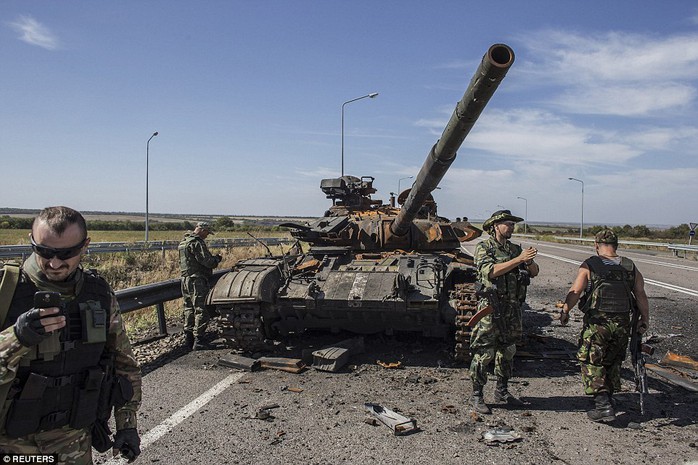 Các tay súng ly khai đứng cạnh một chiếc xe tăng của quân đội Ukraine bị phá hủy bên ngoài TP Luhansk. Ảnh: Reuters