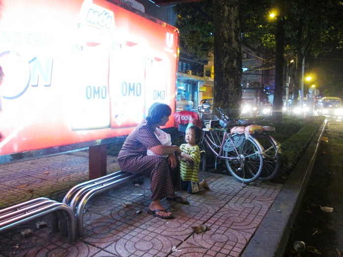 Một đứa trẻ quỳ gối, mếu máo van xin tiền người chờ xe buýt bên đường