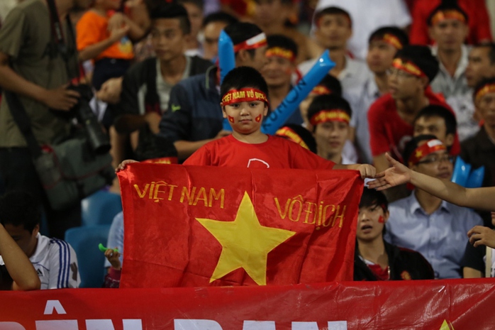 Một em nhỏ cầm lá cờ có hàng chữ Việt Nam vô địch
