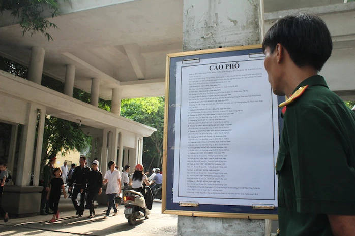 Một cán bộ đứng trước cáo phó ghi tên 18 đồng đội của mình ngoài cổng nhà tang lễ