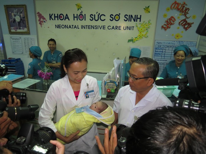 Bé sơ sinh được đưa ra gặp cha trong vòng tay của ThS-BS Phạm Thị Thanh Tâm, Trưởng khoa Hồi sức sơ sinh (trái) và TS-BS Nguyễn Thanh Hùng, Giám đốc BV Nhi Đồng 1