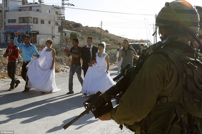 An Israeli soldier stands guard as two Palestinian couples participate in a protest against the Israeli barrier before their wedding in the village of al-Masara, near Bethlehem on July 31, 2009