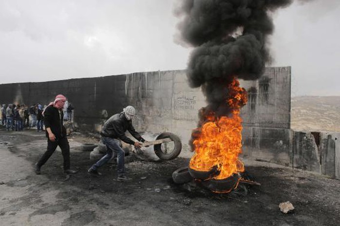 A Palestinian protester places a tyre on a burning pile during clashes with Israeli troops near Israels controversial barrier that separates the West Bank town of Abu Dis from Jerusalem November 17, 2014.  REUTERS-Ammar Awad