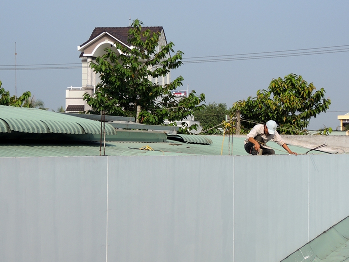 Công nhân leo lên nóc nhà kho để tháo dỡ mái tôn. Ảnh: D.M.Phương