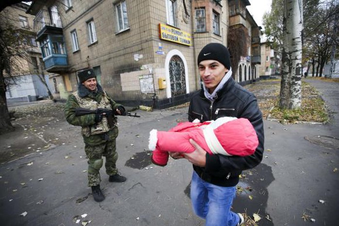 Một người đàn ông bế đứa bé đi ngang qua một tay súng ly khai ở Donetsk. Ảnh: REUTERS