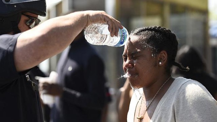 Một sĩ quan cảnh sát Baltimore rửa mặt cho một người phụ nữ bị trúng hơi cay. Ảnh: Reuters