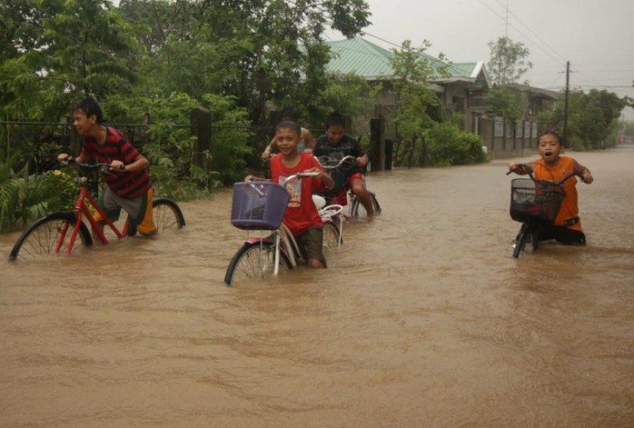 Trẻ em thị trấn Baccara, tỉnh Ilocos Norte, Philippines đạp xe trên con đường ngập nước do bão Goni hôm 21-8. Ảnh: EPA