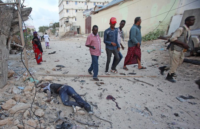 Somalis walk past a dead  civilian  outside the hotel who was killed  after a car bomb that was detonated at the gate of a hotel in Mogadishu, Somalia , Friday, March, 27, 2015,, A Somali police official says a suicide bomber has detonated his explosives-laden car at the gate of a hotel popular with government officials in Mogadishu. Capt. Mohamed Hussein says gunfire could be heard inside the Maka-Mukarramah Hotel, but it was not clear if any gunmen had managed to penetrate the hotels gate( AP Photo/Farah Abdi Warsameh)
