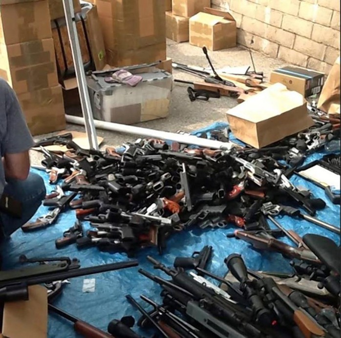 Police inspect some of the 1,200 guns found in the condo of a man who was decomposing in a car down the street for about two weeks.