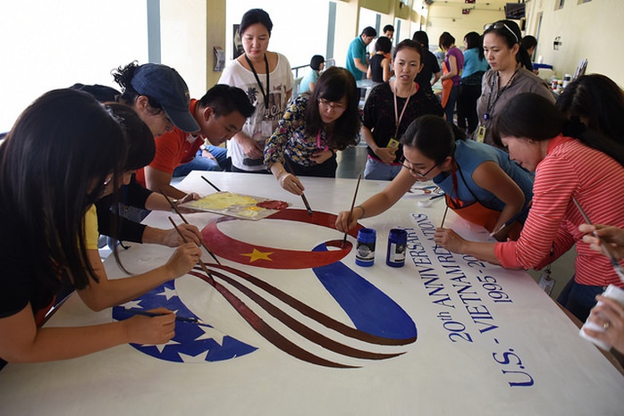 Các nhân viên của Tổng lãnh sự Mỹ tại TPHCM cùng các họa sĩ đang vẽ bức trang sơn dầu khắc họa logo được thiết kế để kỷ niệm 20 năm ngày thiết lập lại quan hệ ngoại giao giữa hai nước. Ảnh: Tổng lãnh sự Mỹ tại TPHCM cung cấp