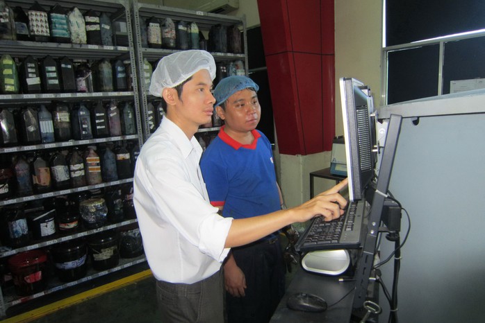 Anh Lê Quốc Dũng (trái), phụ trách quản lý hệ thống chất lượng và môi trường Công ty CP In Nhãn hàng An Lạc, hướng dẫn công nhân thao tác trên máy tính