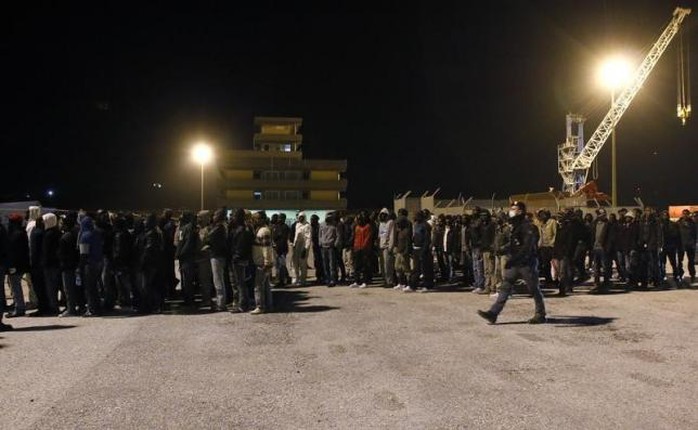 Cảnh sát hộ tống người di cư khi họ được đưa lên bờ từ một tàu hải quân tại cảng Sicily - Ý vào tháng 3. Ảnh: Reuters
