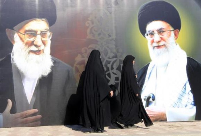 Iraqi women walk past a poster depicting images of Shiite Irans Supreme Leader Ayatollah Ali Khamenei at al-Firdous Square in Baghdad February 12, 2014. \REUTERS/Ahmed Saad