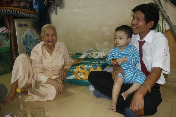 Bé Bo trong vòng tay của tài xế Hồ Minh Thuận. Người ngồi bên trái là bà Nguyễn Thị Em - bà cố của bé Bo.