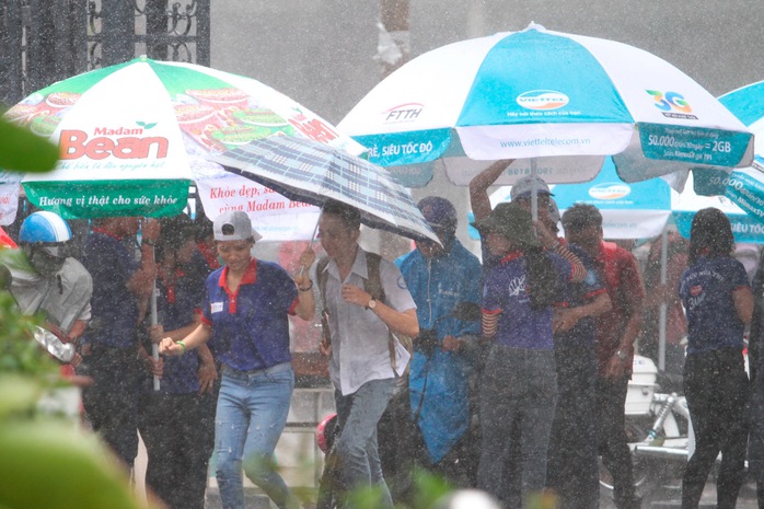 Sinh viên tình nguyện tại Trường ĐH Sư phạm TP HCM chịu ướt để đưa thí sinh vào điểm thi trong trời mưa tầm tã chiều ngày 1-7 Ảnh: Hoàng Triều