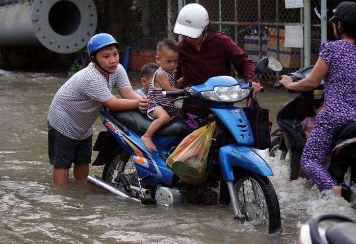 Hai em bé phụ mẹ đẩy xe máy để vượt qua vùng nước ngập.