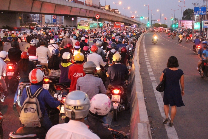 Một người phụ nữ quyết định rời xe máy, đi bộ chờ người thân ở bên kia ngã tư.