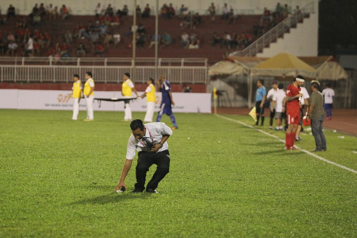 Một thành viên BTC sân vào nhặt chai nước mà tiền vệ Hồng Việt ném xuống để phản ứng HLV Alain Fiard